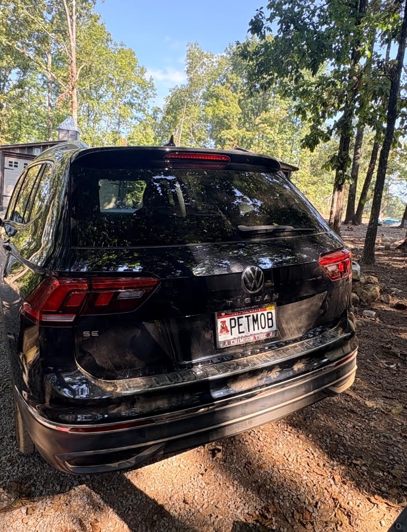 The Alabama Pet Transport Services vehicle: a black SUV with an Alabama PETMOB license plate, parked outside on a wooded gravel drive.